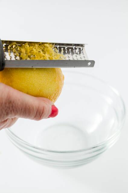 zesting a lemon with a microplane zester into a glass bowl