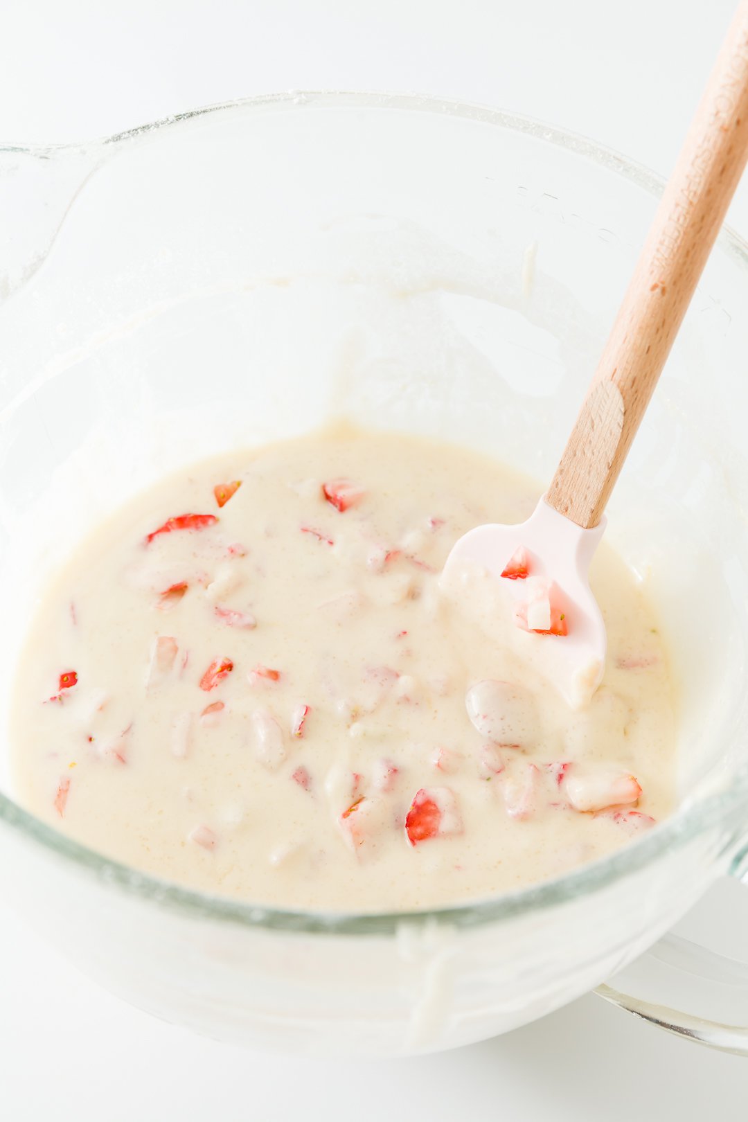 stirring strawberries into strawberry cupcake batter with a pink spatual