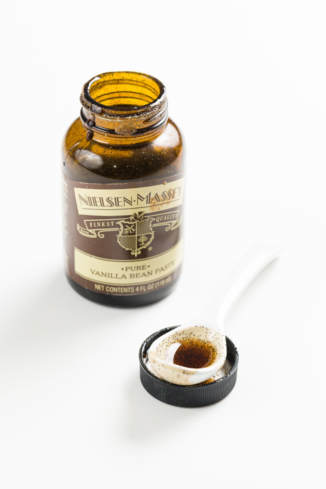 a spoon with vanilla bean paste in the foreground with a bottle of Nielsen-Massey vanilla bean paste in the background