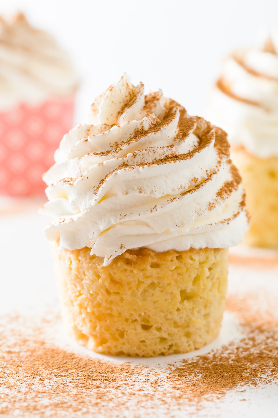 Close up of a tres leches cupcake with a couple other cupcakes in the background