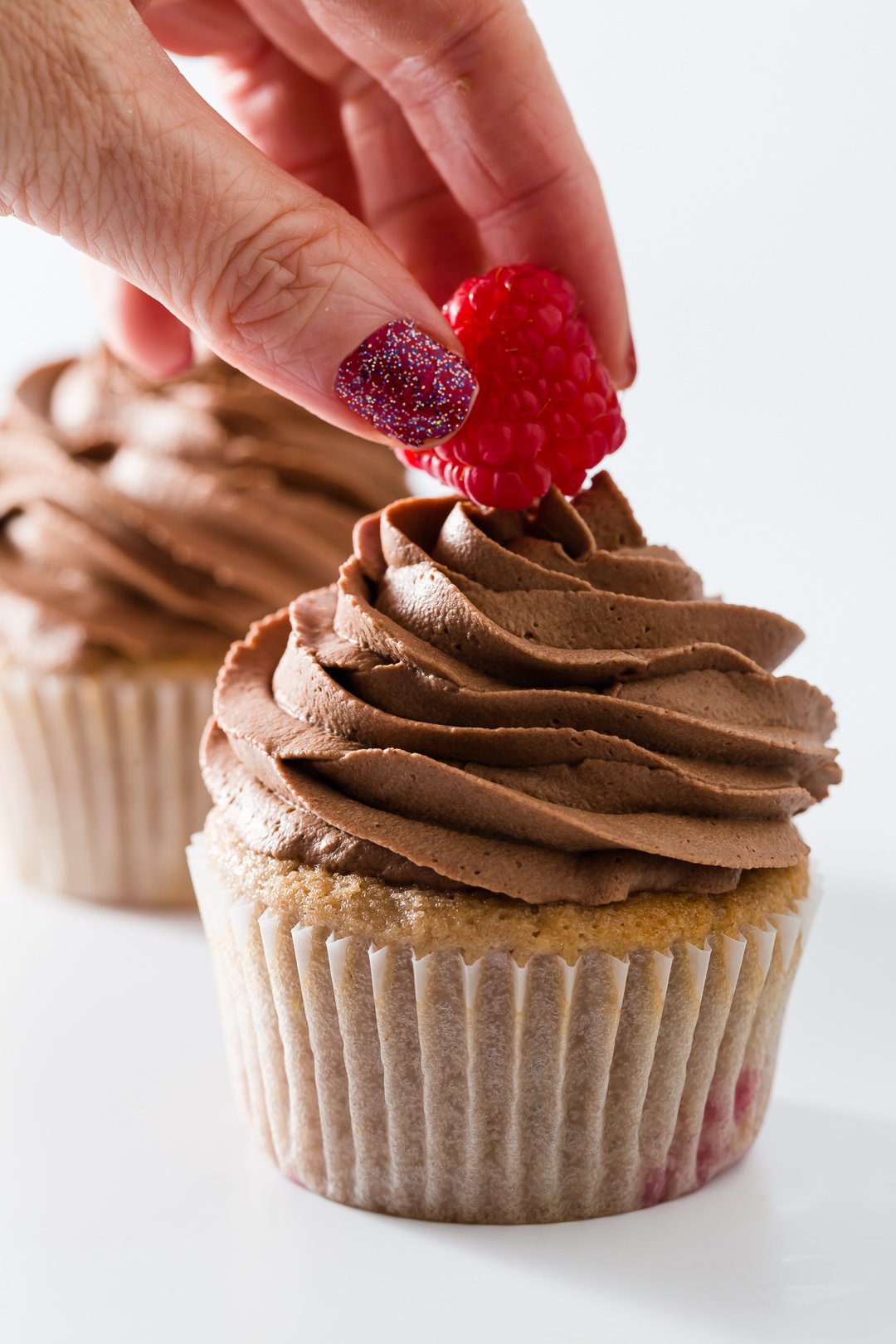 Placing a raspberry on top of chocolate whipped cream frosting