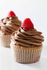 Two raspberry cupcakes frosted with chocolate whipped cream and topped with fresh raspberries