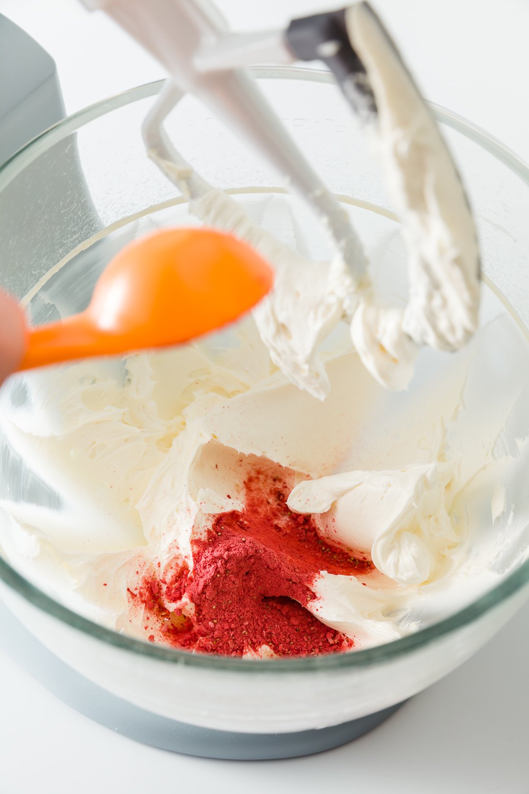 a view into an electric stand mixer bowl where strawberry powder is being added to cream cheese whipped with butter