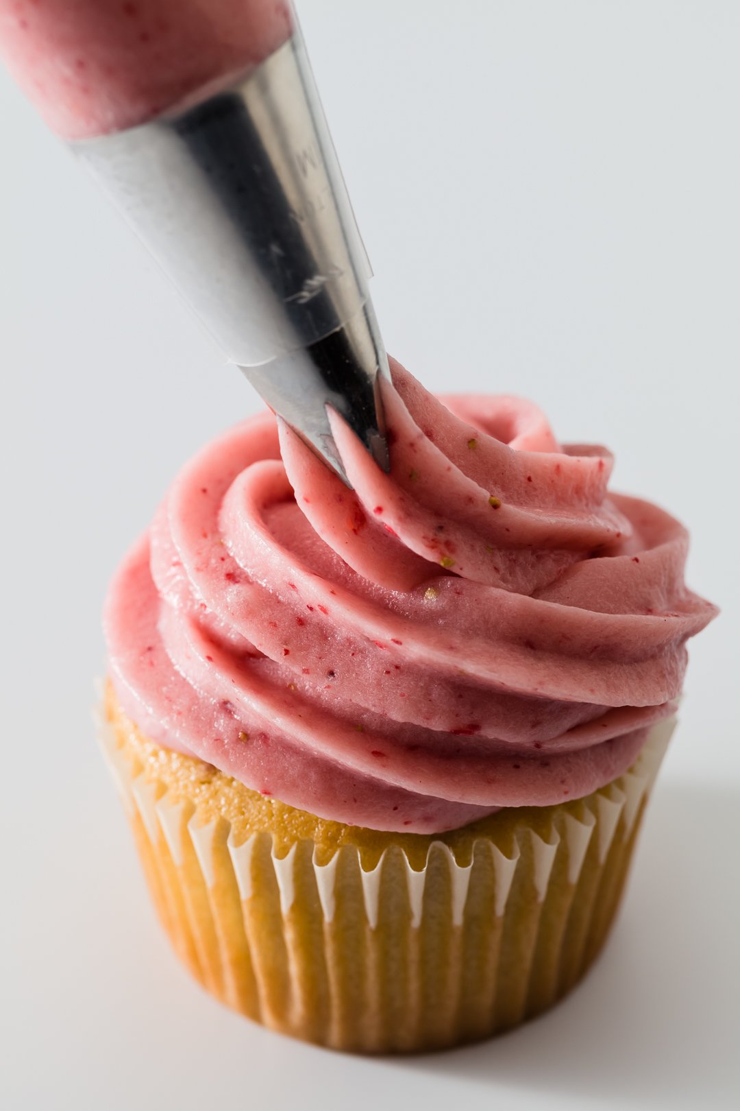 a piping tip frosting a strawberry cupcakes with pink strawberry cream cheese frosting