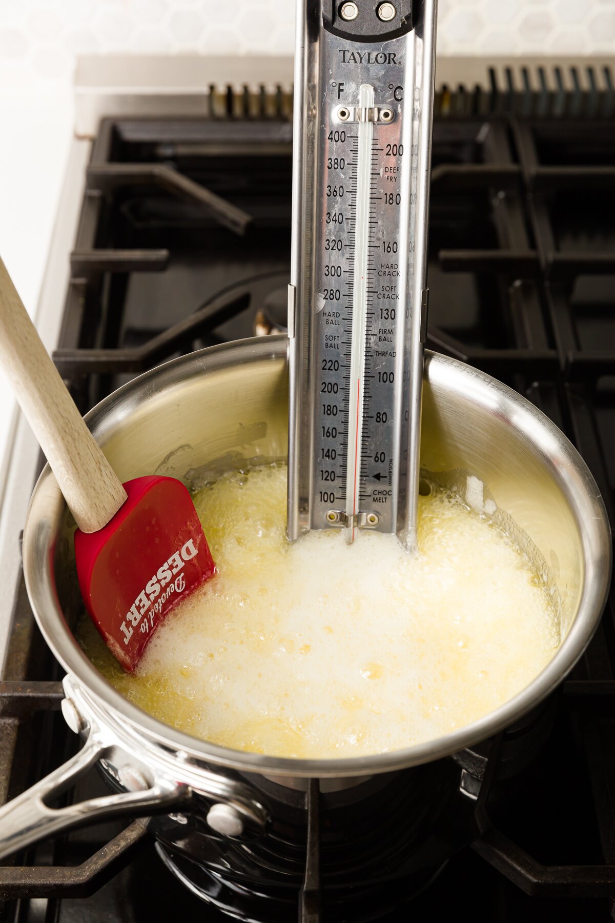 Pot of bubbling sugar with a red spatula and a candy thermometer