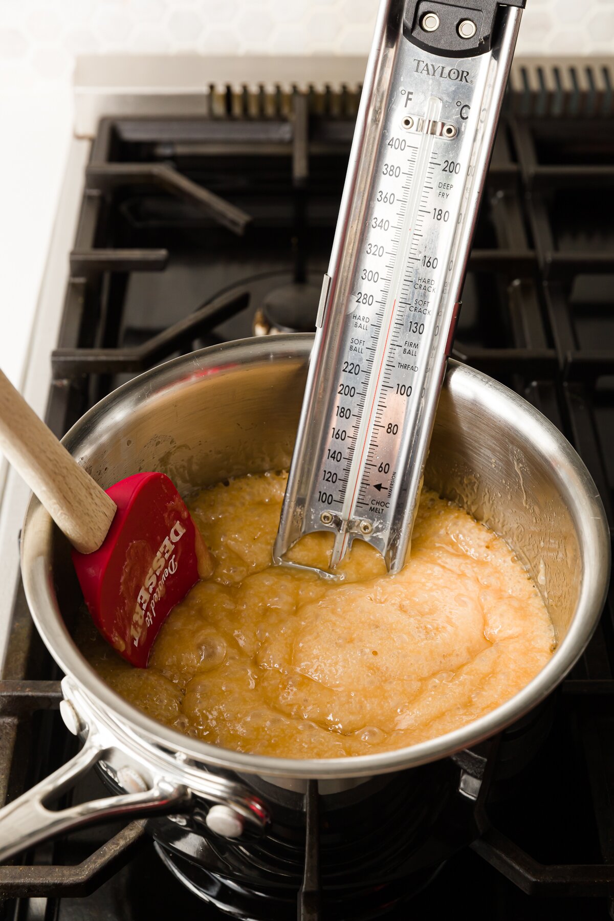 Golden toffee in a pot still bubbling with a candy thermometer and a spatula