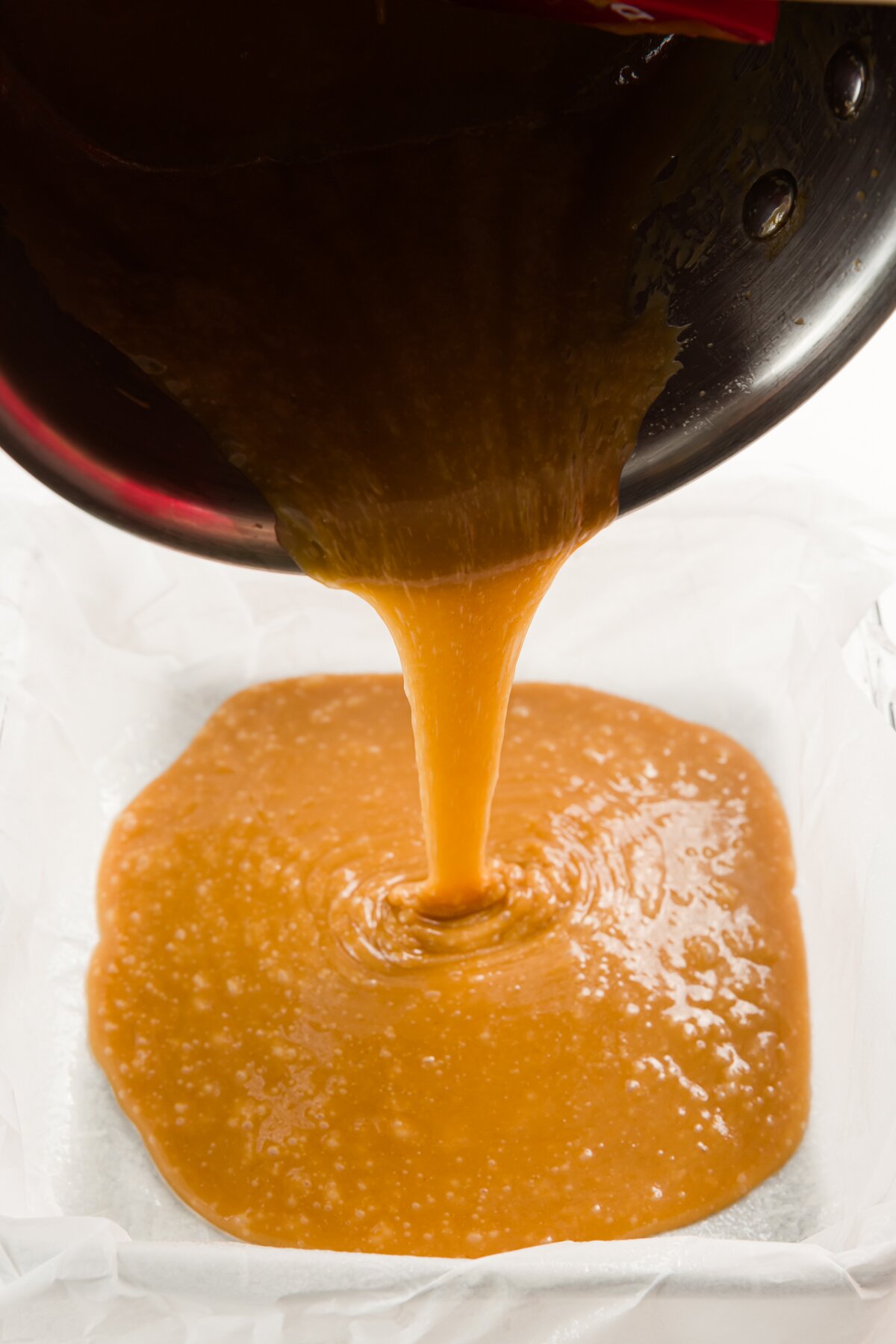 Pouring toffee into a glass pan with parchment paper in it
