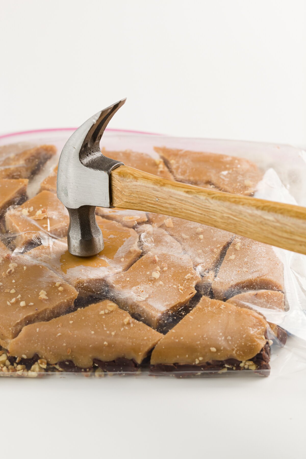 Upside-dwon ziplock bag of toffee broken into pieces being hit with a hammer