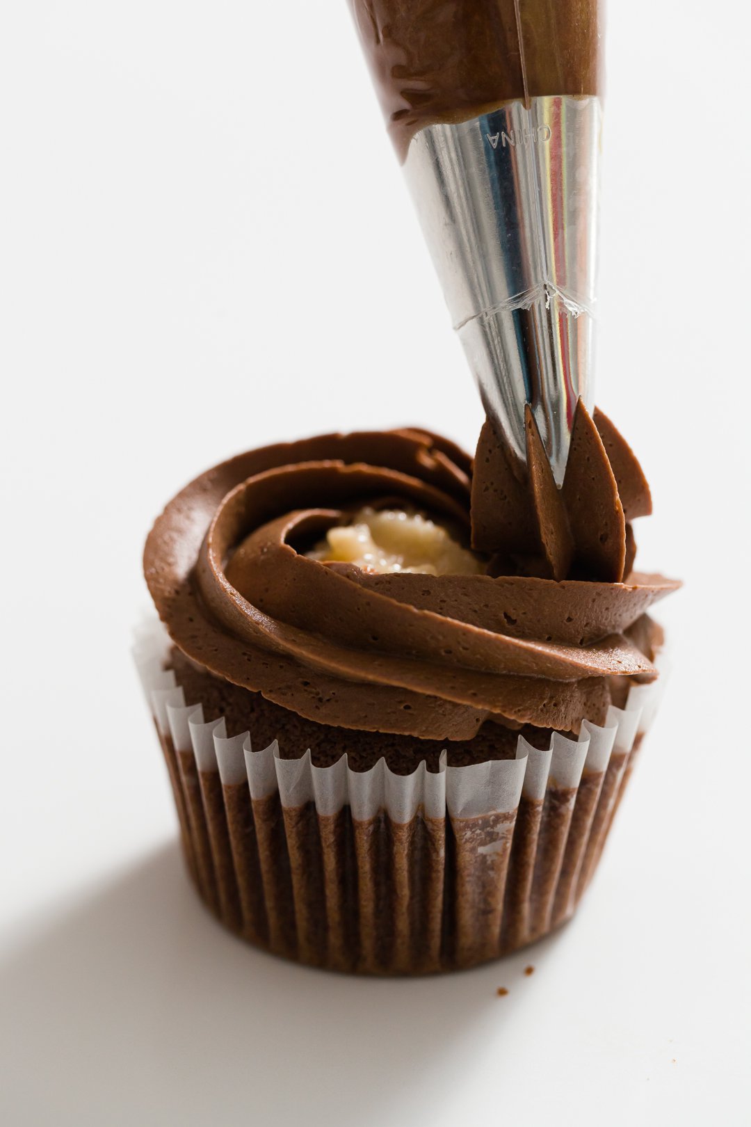 Piping chocolate buttercream over filled cupcake