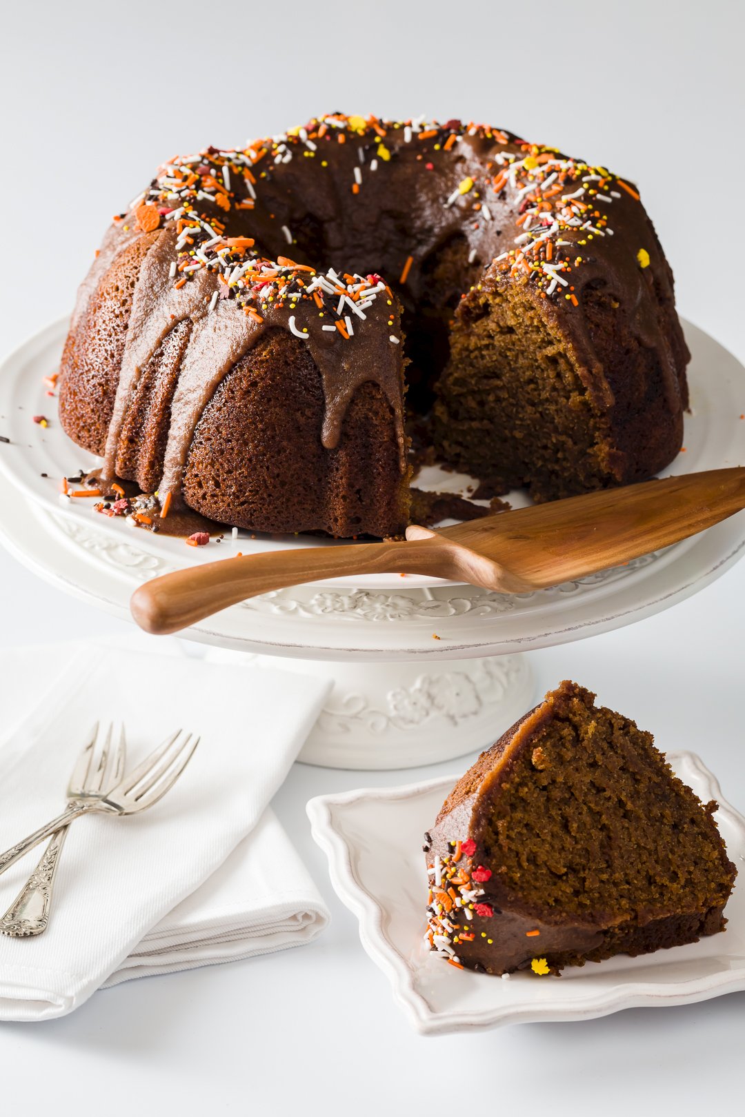 pumpkin spice cake sitting on a cake stand with a slice removed in the foreground.