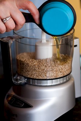 adding olive oil to a food processor full of toasted sesame seeds