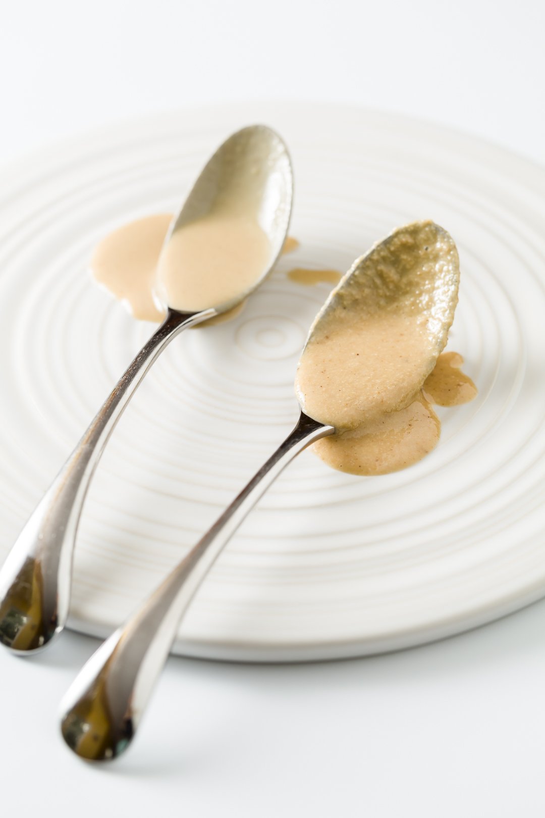 store-bought tahini and homemade tahini on spoons to show textural differences