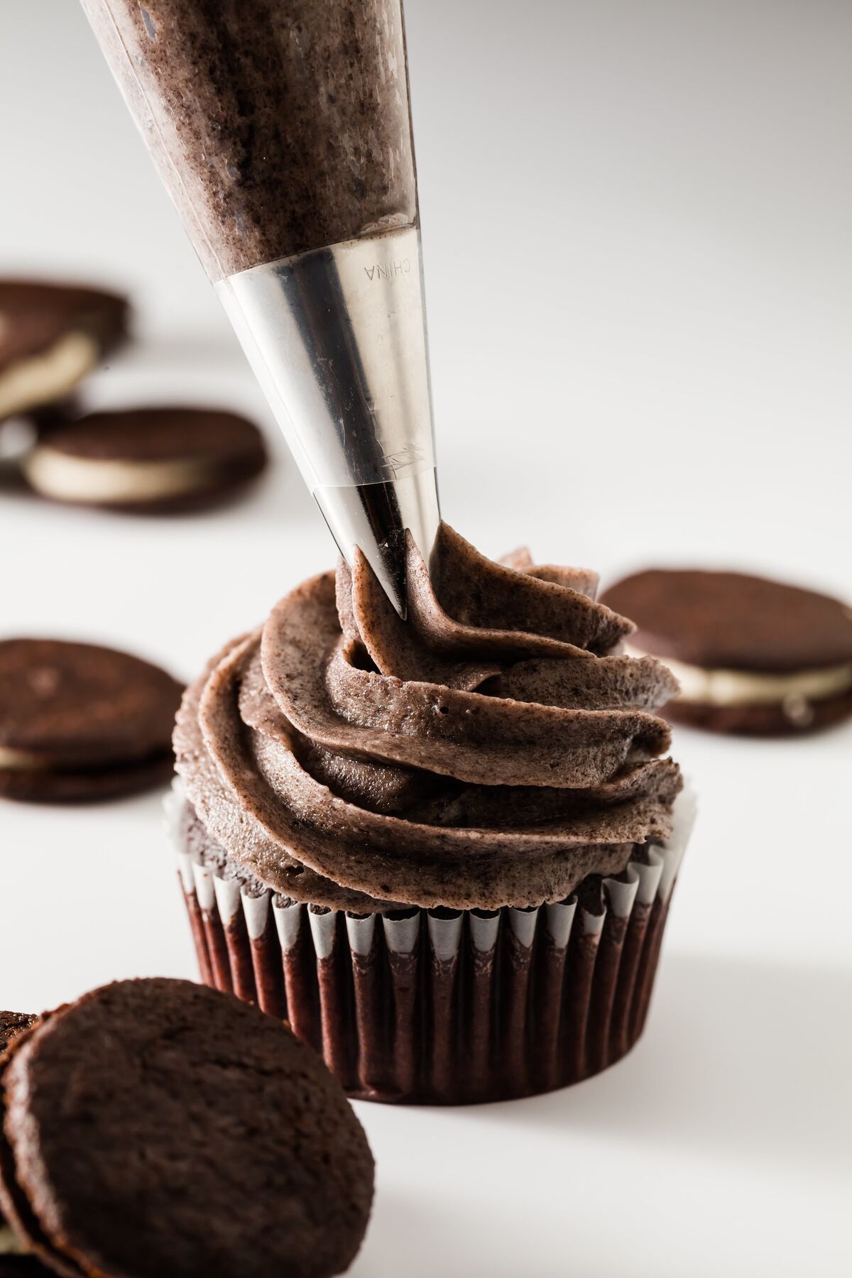 Oreo cookies and cream frosting being piped onto a cupcake