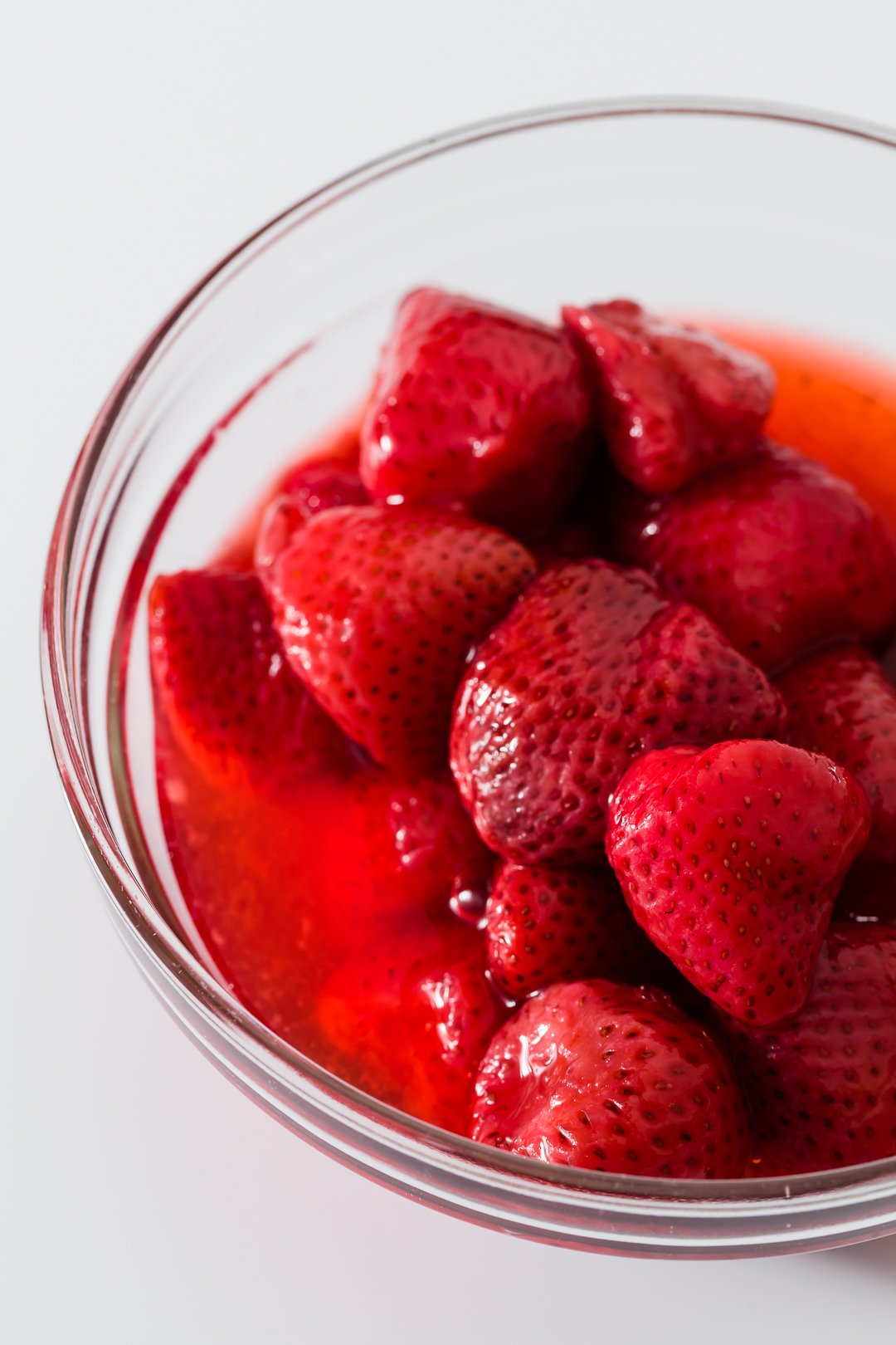 defrosted frozen strawberries in a glass bowl with lots of strawberry juice