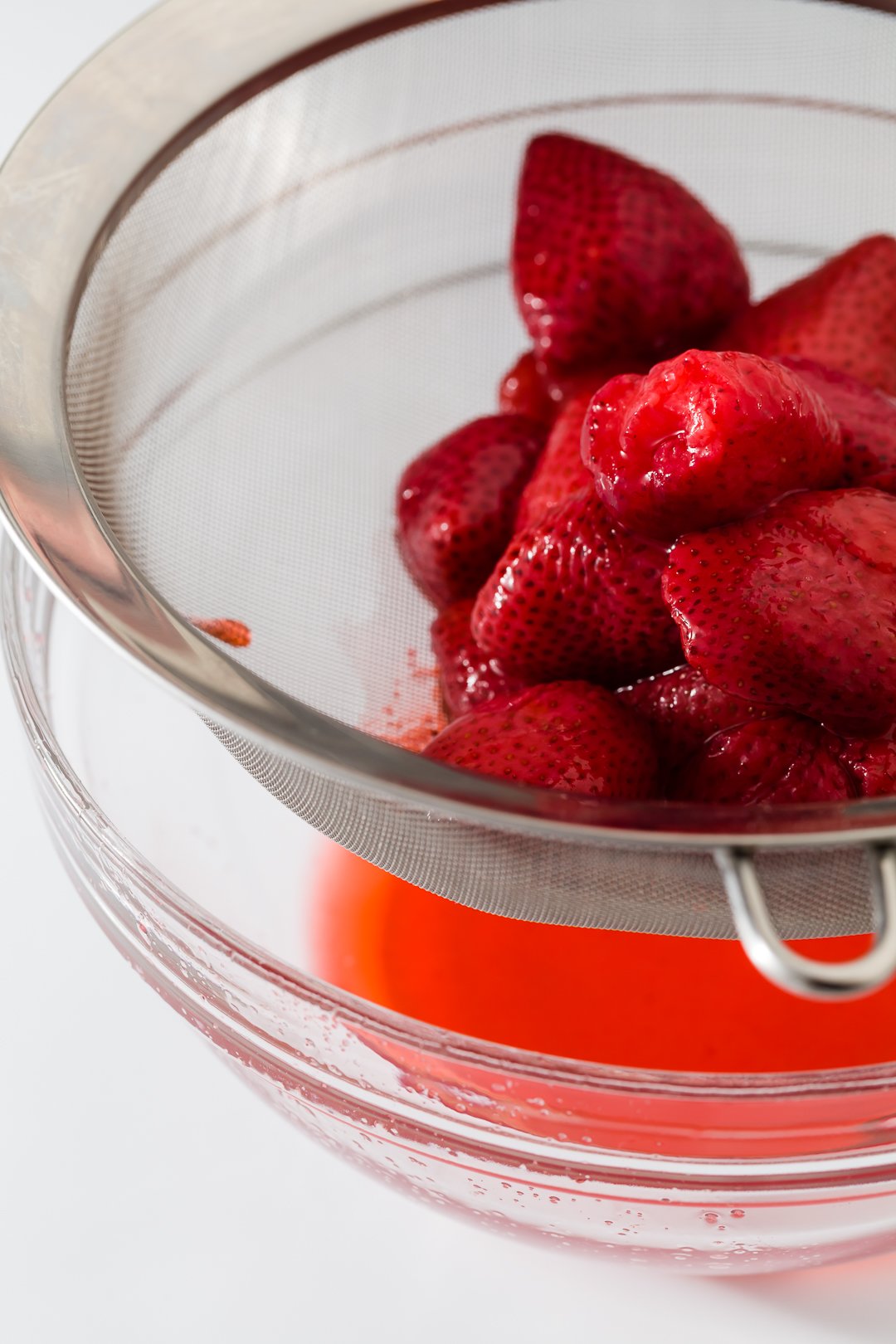 strawberry juice being strained off of strawberries using a sieve