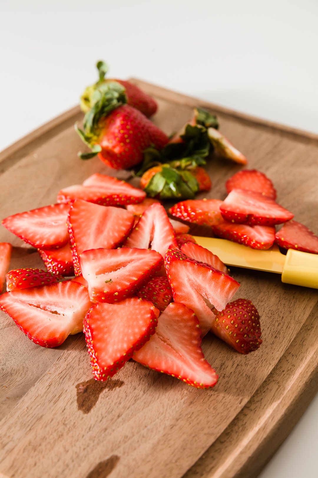 a wooden cutting board with sliced strawberries and a yellow knife