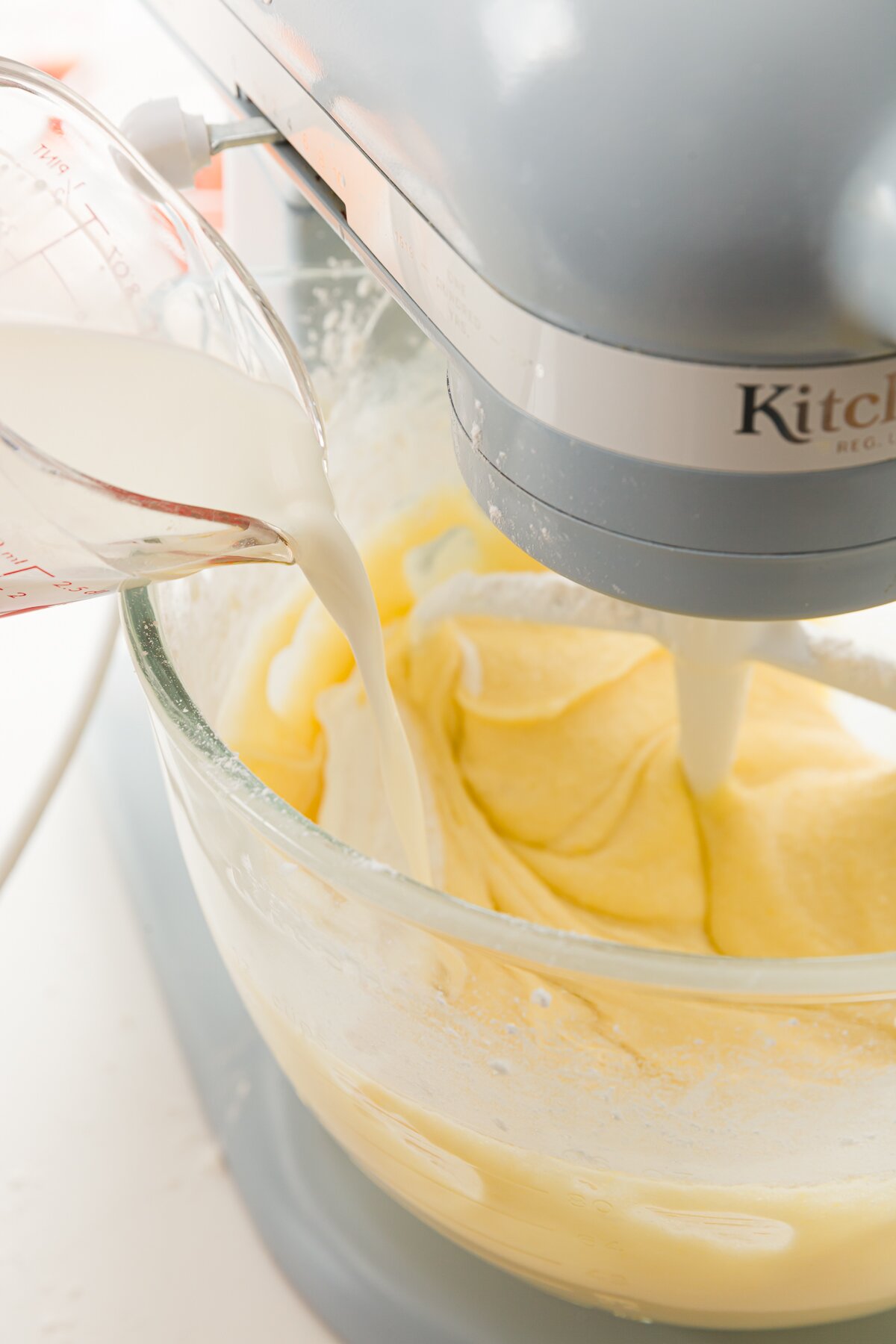 Pouring mixing into a kitchenaid mixer bowl filled with smooth batter
