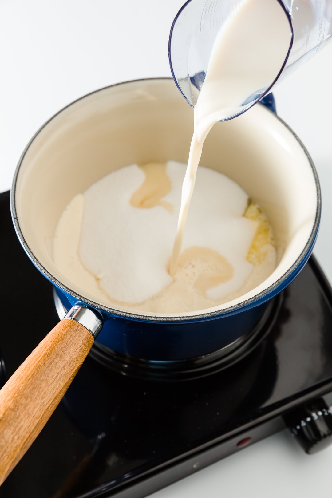 Adding evaporated milk to a saucepan filled with butter and sugar