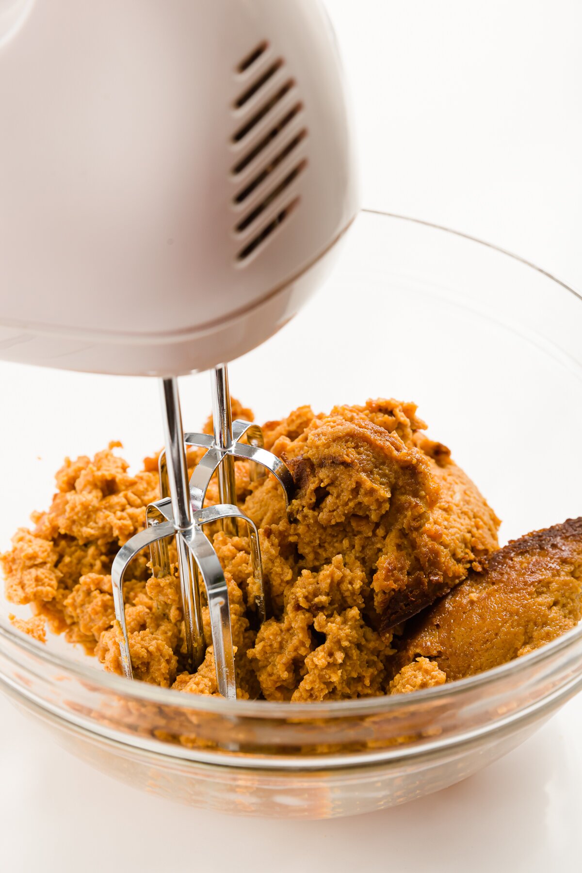 Mixing pumpkin pie in a clear mixing bowl with a white hand mixer