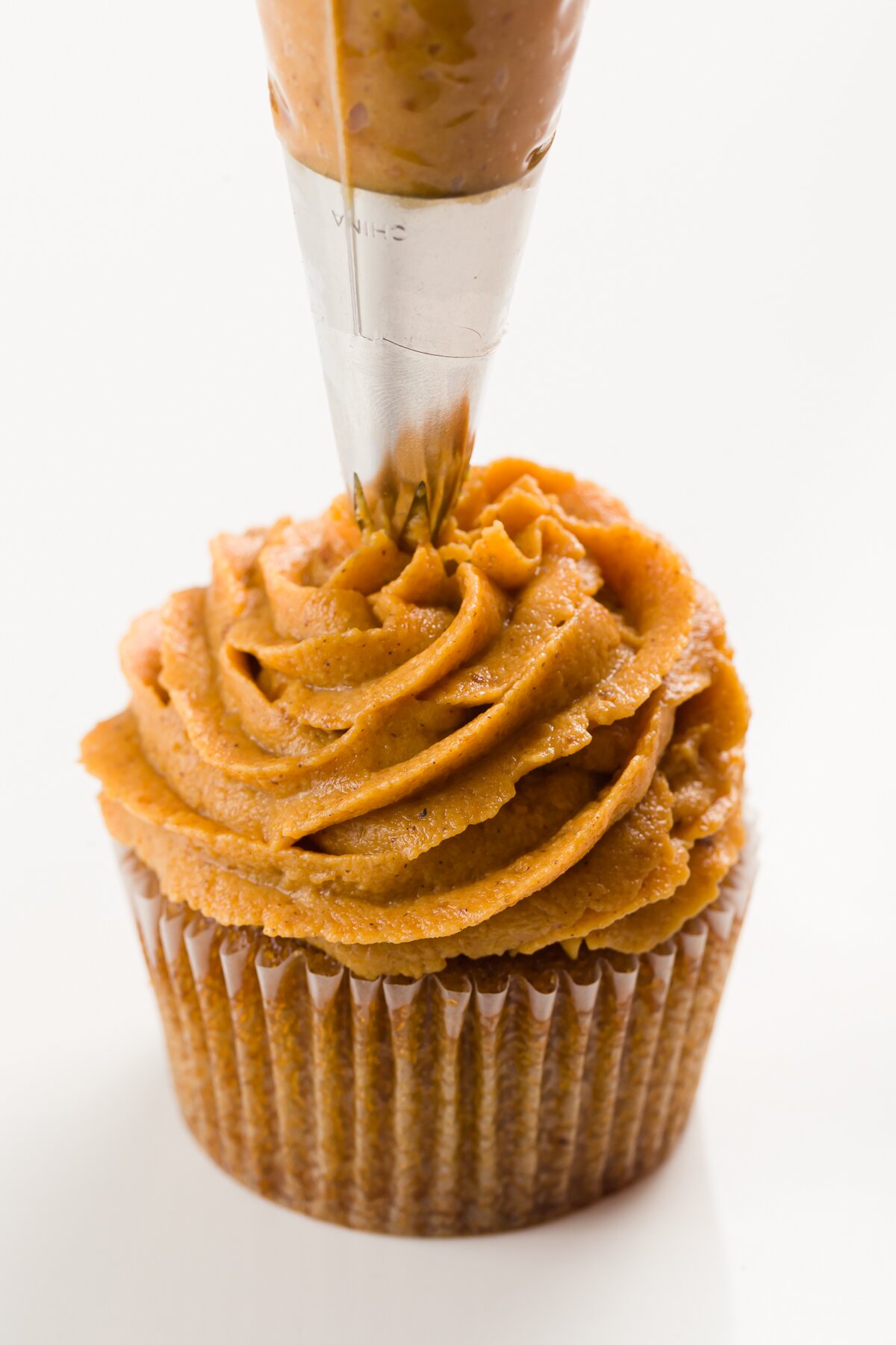 Piping pumpkin frosting onto a cupcake