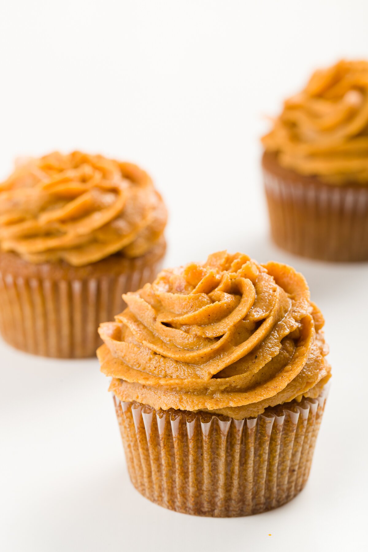 Three cupcakes on a white background frosted with pumpkin frosting