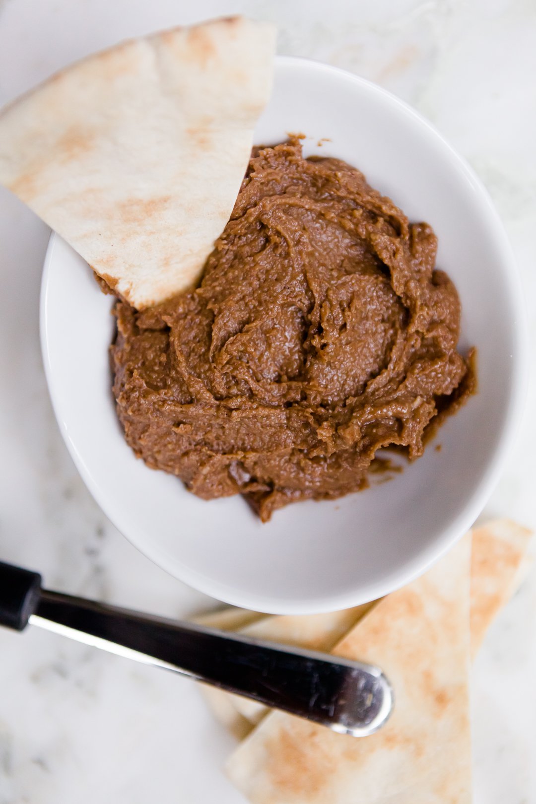 Chocolate hummus in a bowl surrounded by fresh pita bread