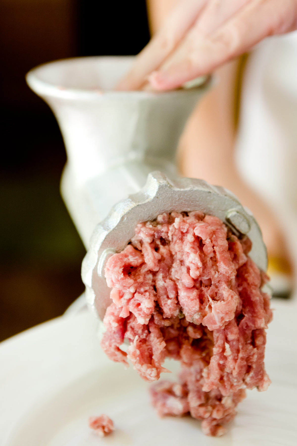 tight shot of Stef's hand forcing pork shoulder through a hand-operated meat grinder