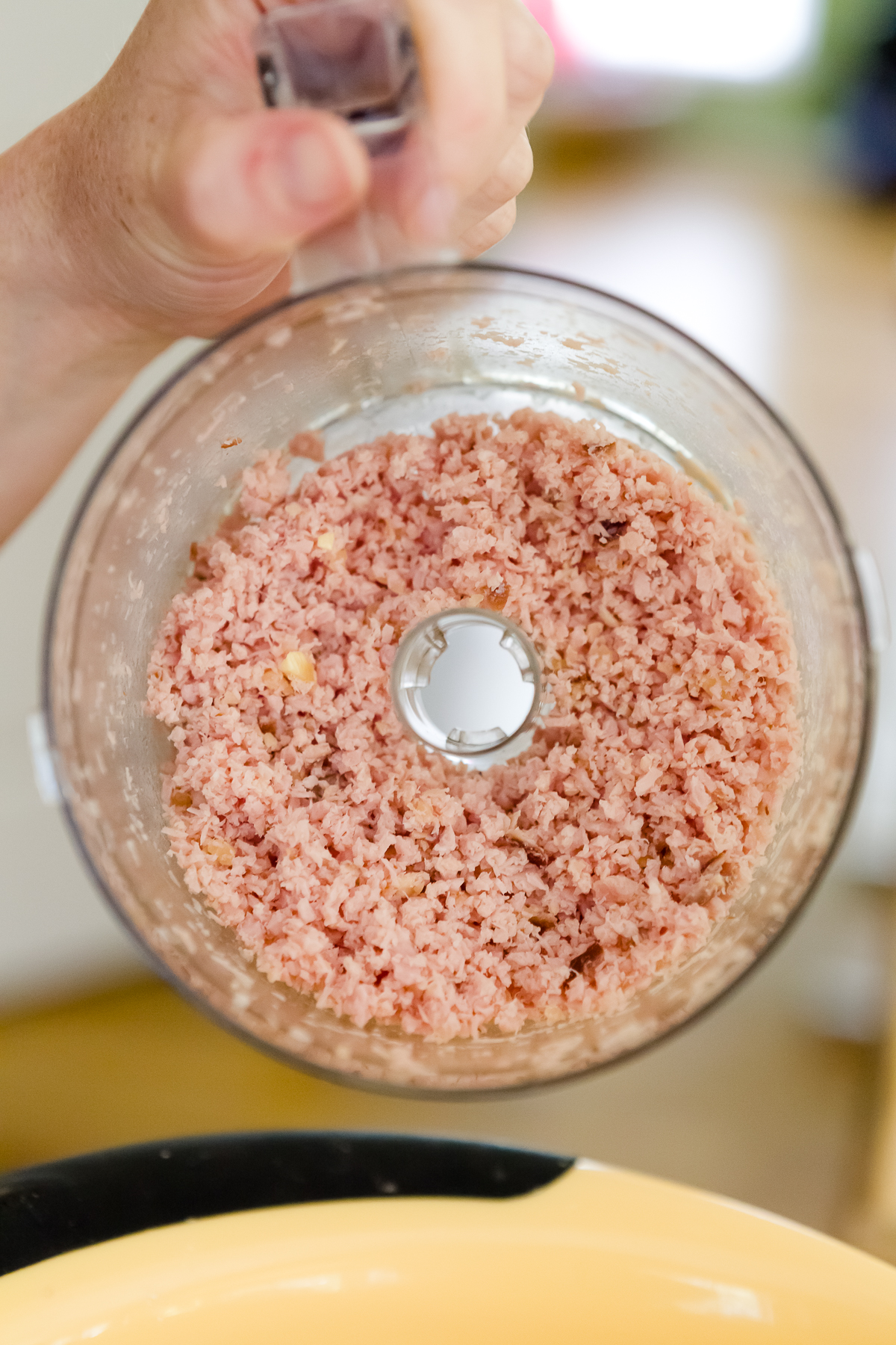 Stef holding up the bowl of a food processor to show diced ham and garlic