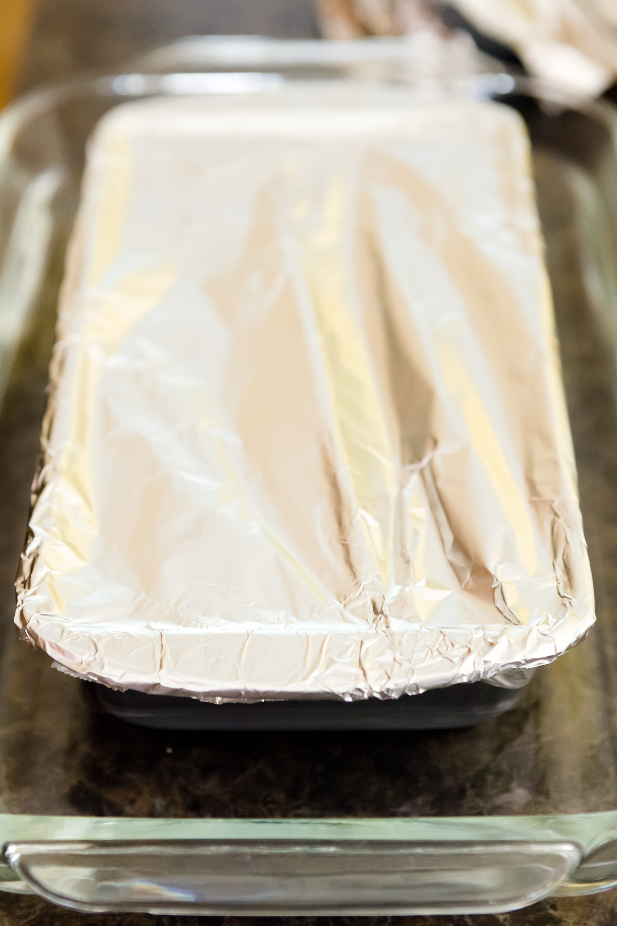 view of a covered loaf pan containing raw homemade Spam in a glass baking dish 3/4 full of water