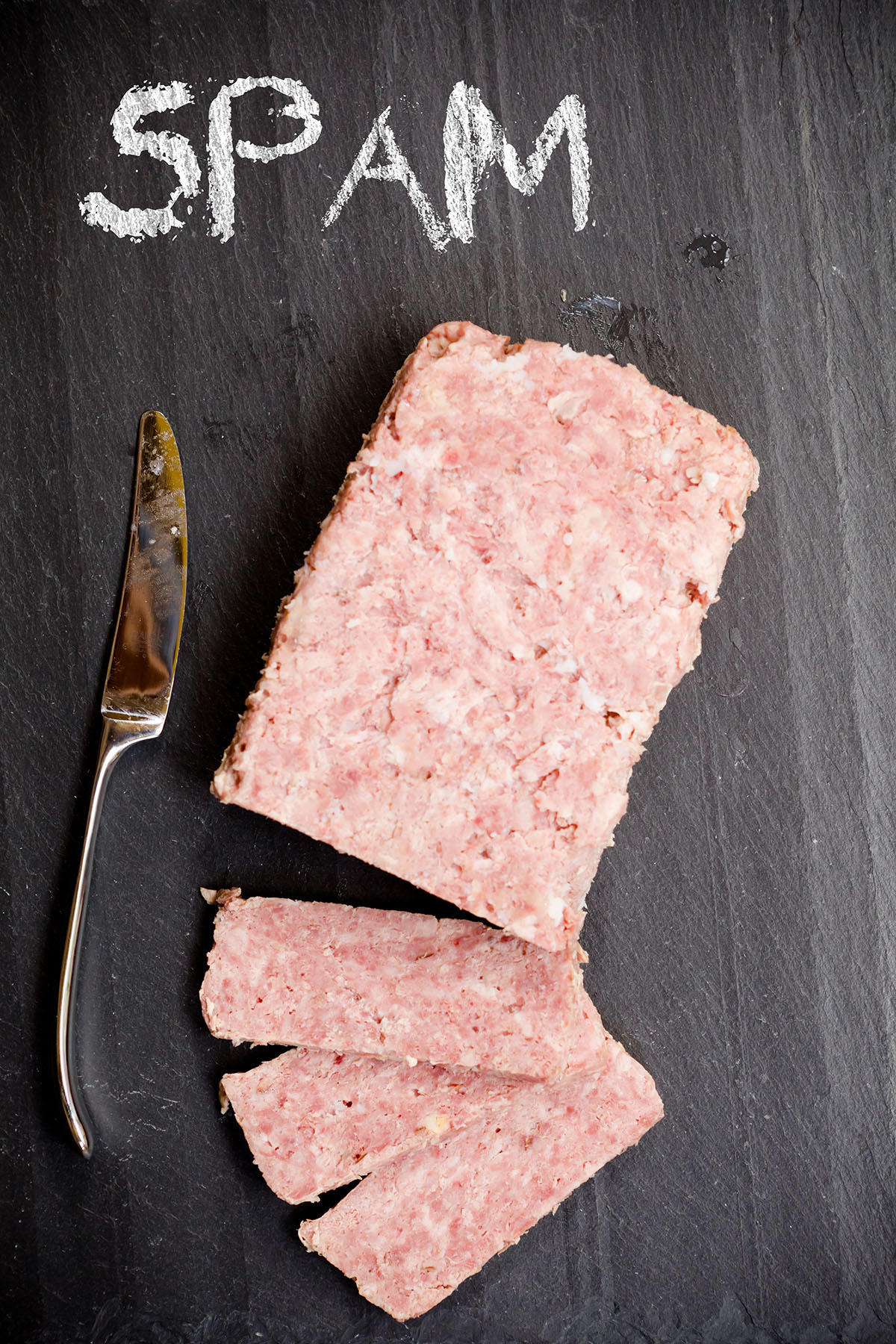 overhead view of homemade Spam loaf with several slices on a slate board