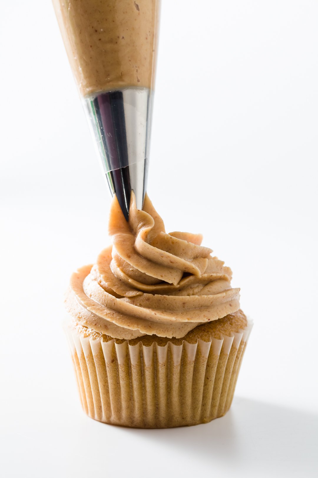 Peanut butter frosting being piped onto cupcakes