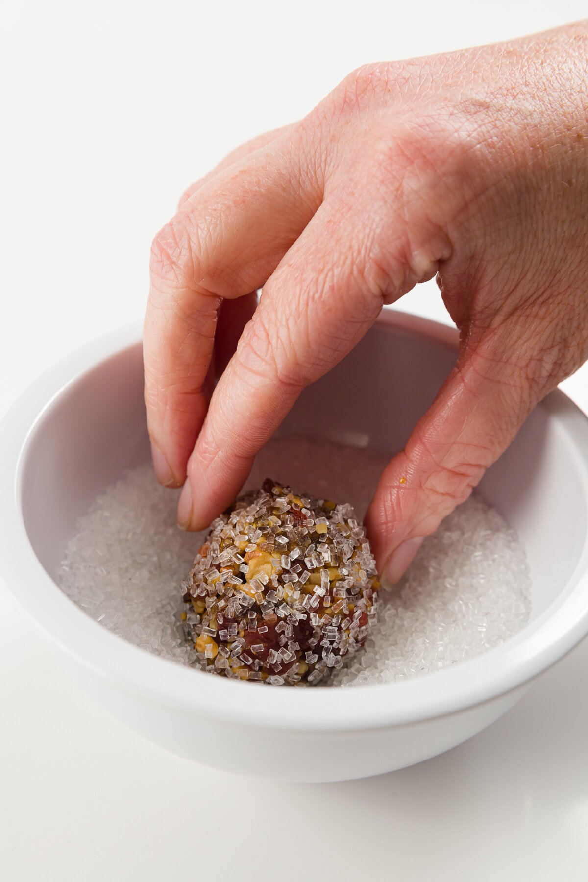 Rolling sugar plum ball in white sanding sugar in a small white bowl