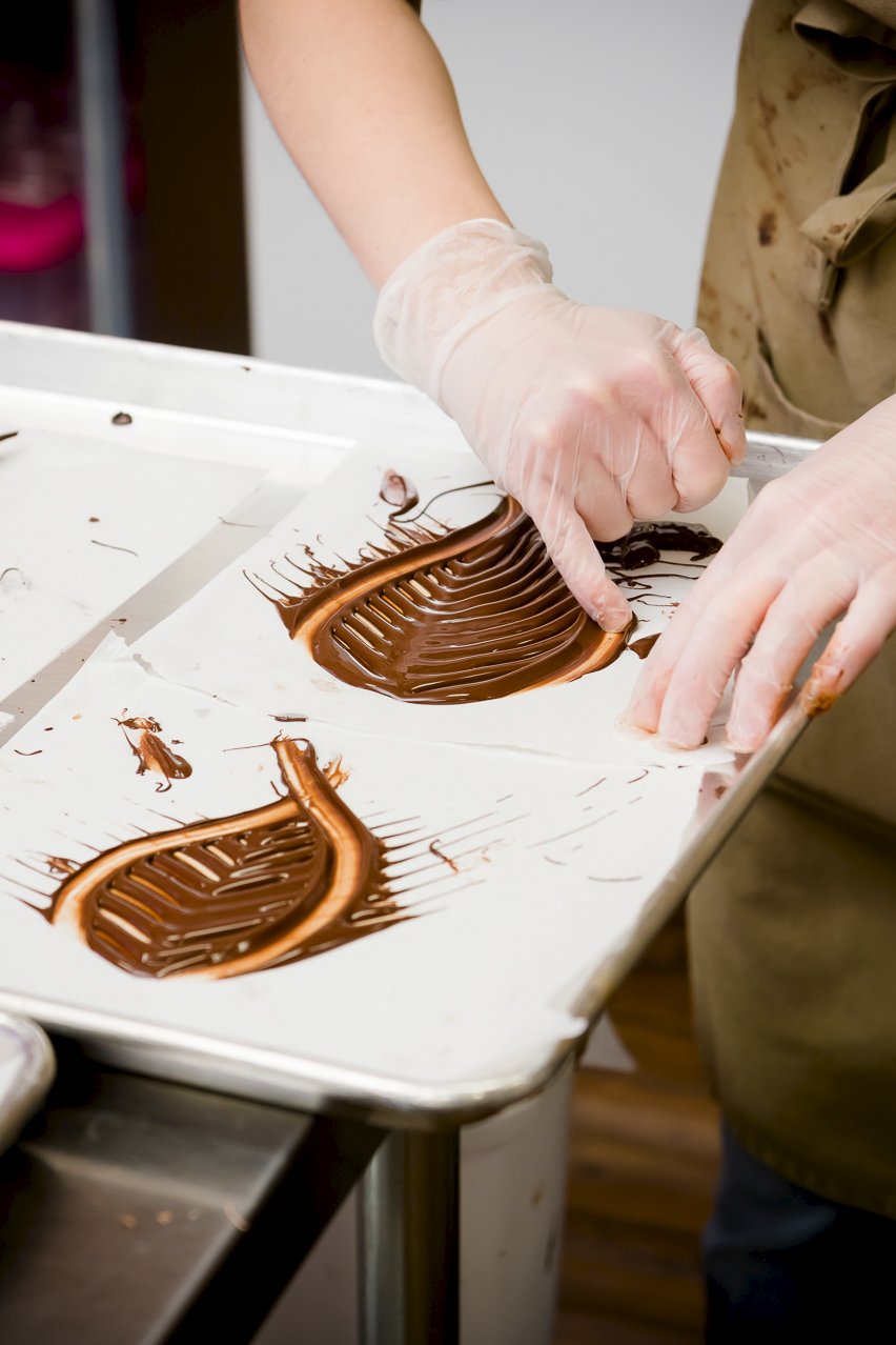 Person running her pinky through chocolate to shape the leaves.