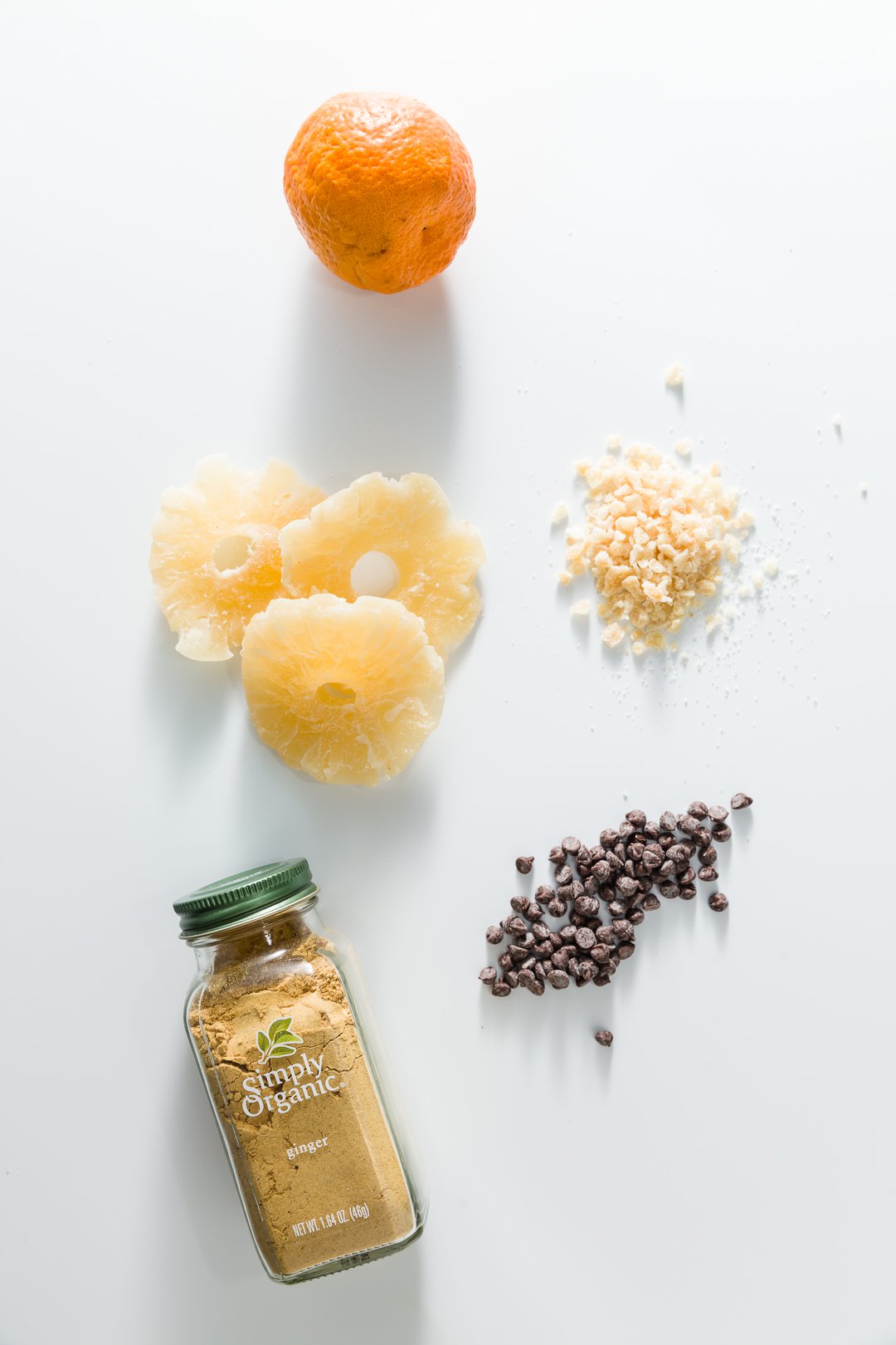 a spice jar, chocolate chips, dried pineapple, crystallized ginger, and an orange