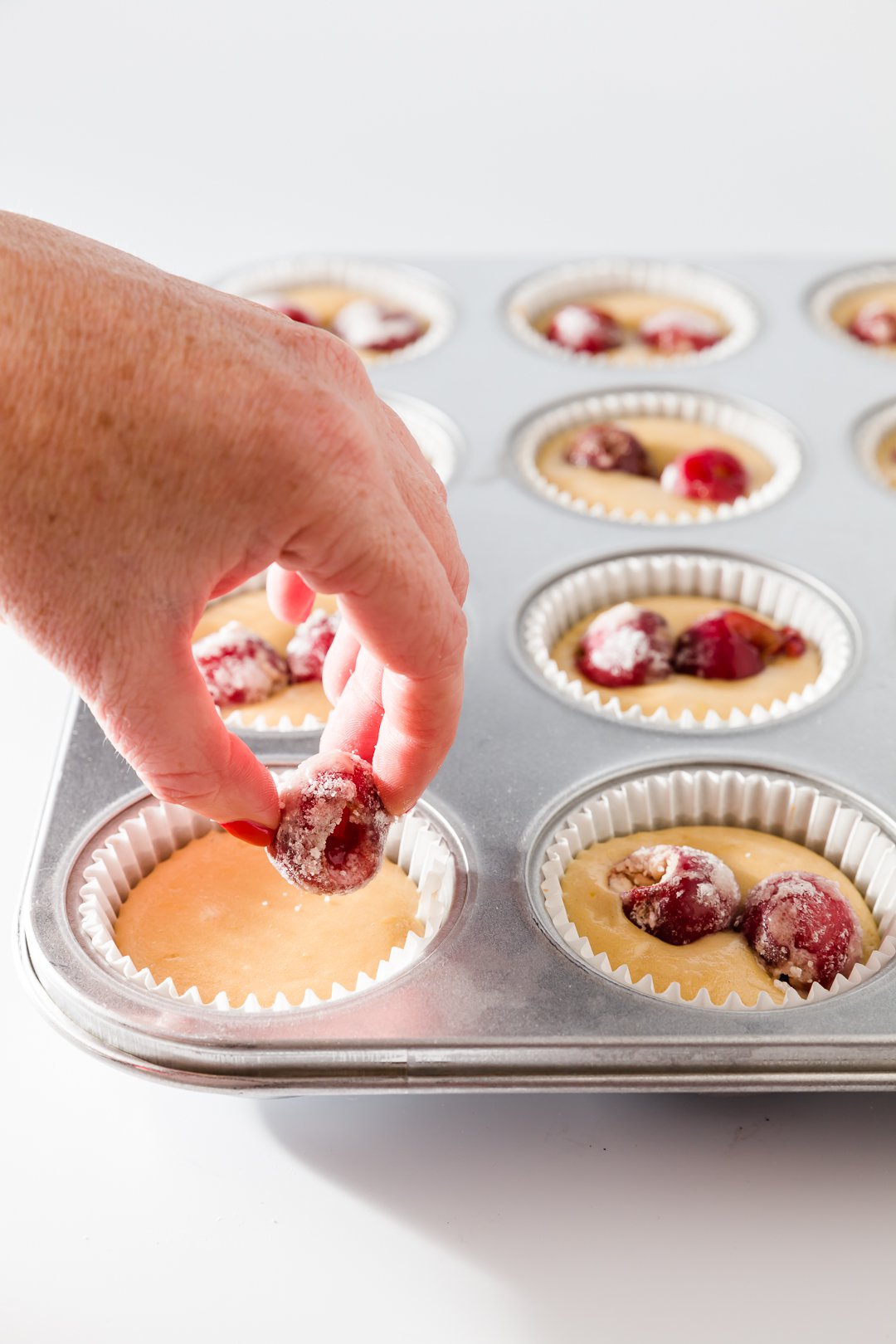 Adding cherries to cupcakes tins