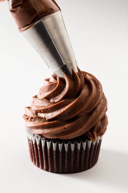 Chocolate cream cheese frosting being piped onto a chocolate cupcake