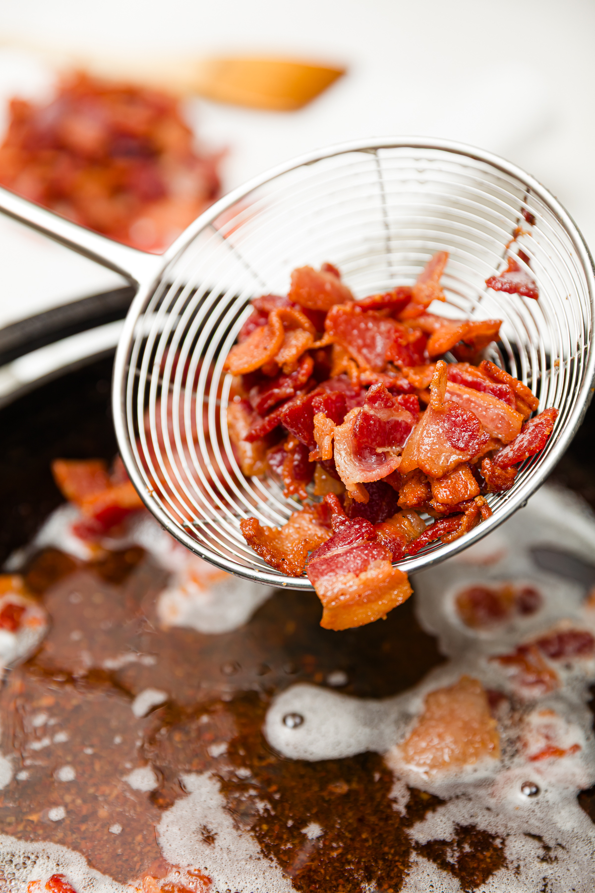 Removing bacon from the pan with a strainer.