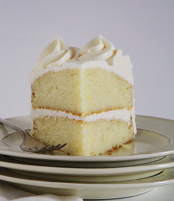 a slice of vanilla cake frosted with vanilla frosting, on a cream plate