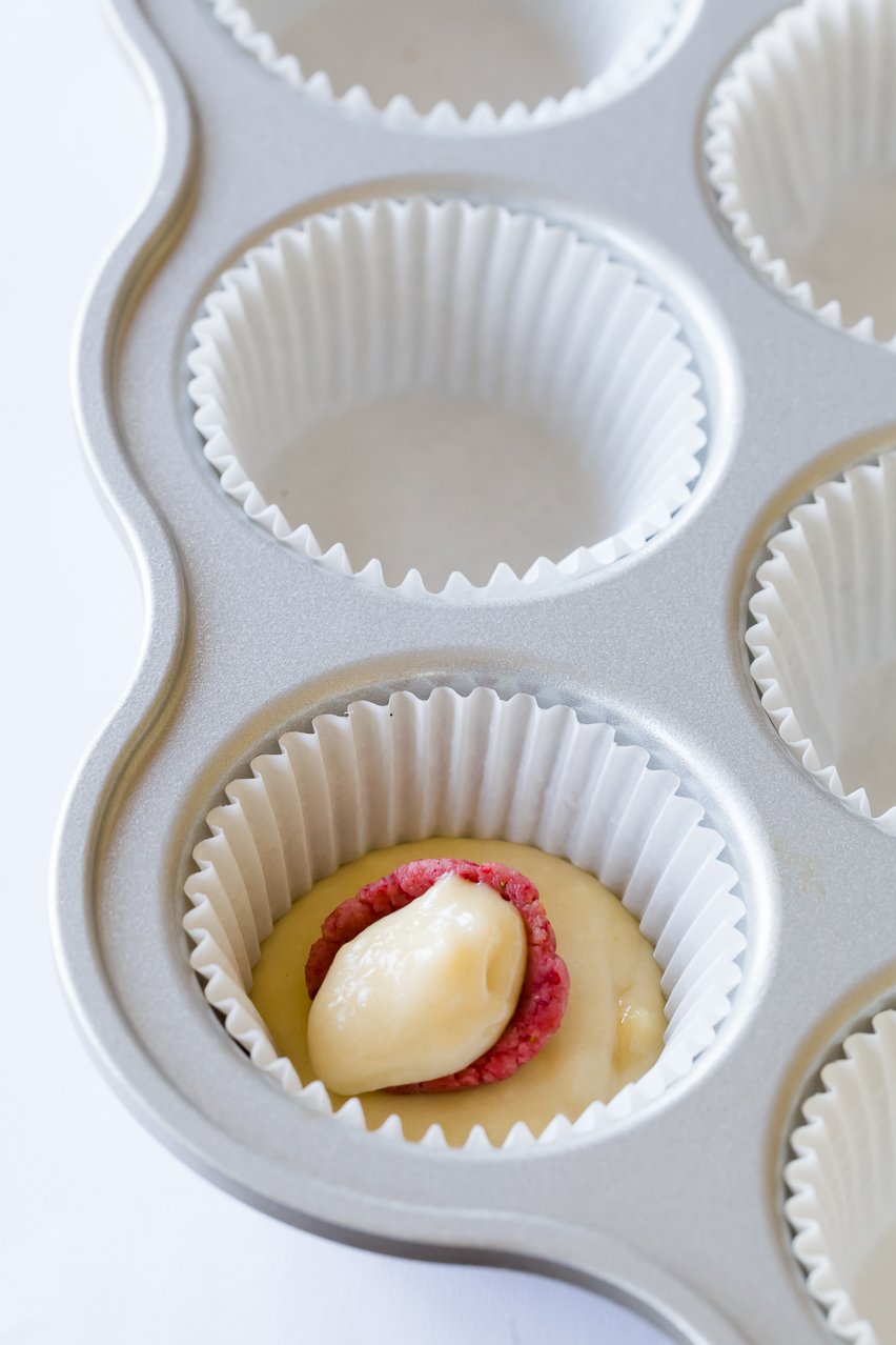 A dollop of batter placed over the red surprise-inside bunny inside of a cupcake liner partially filled with batter