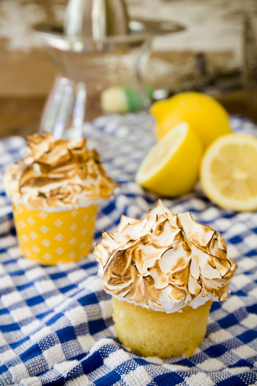 Two mile-high lemon meringue cupcakes with lemons on a checkered tablecloth