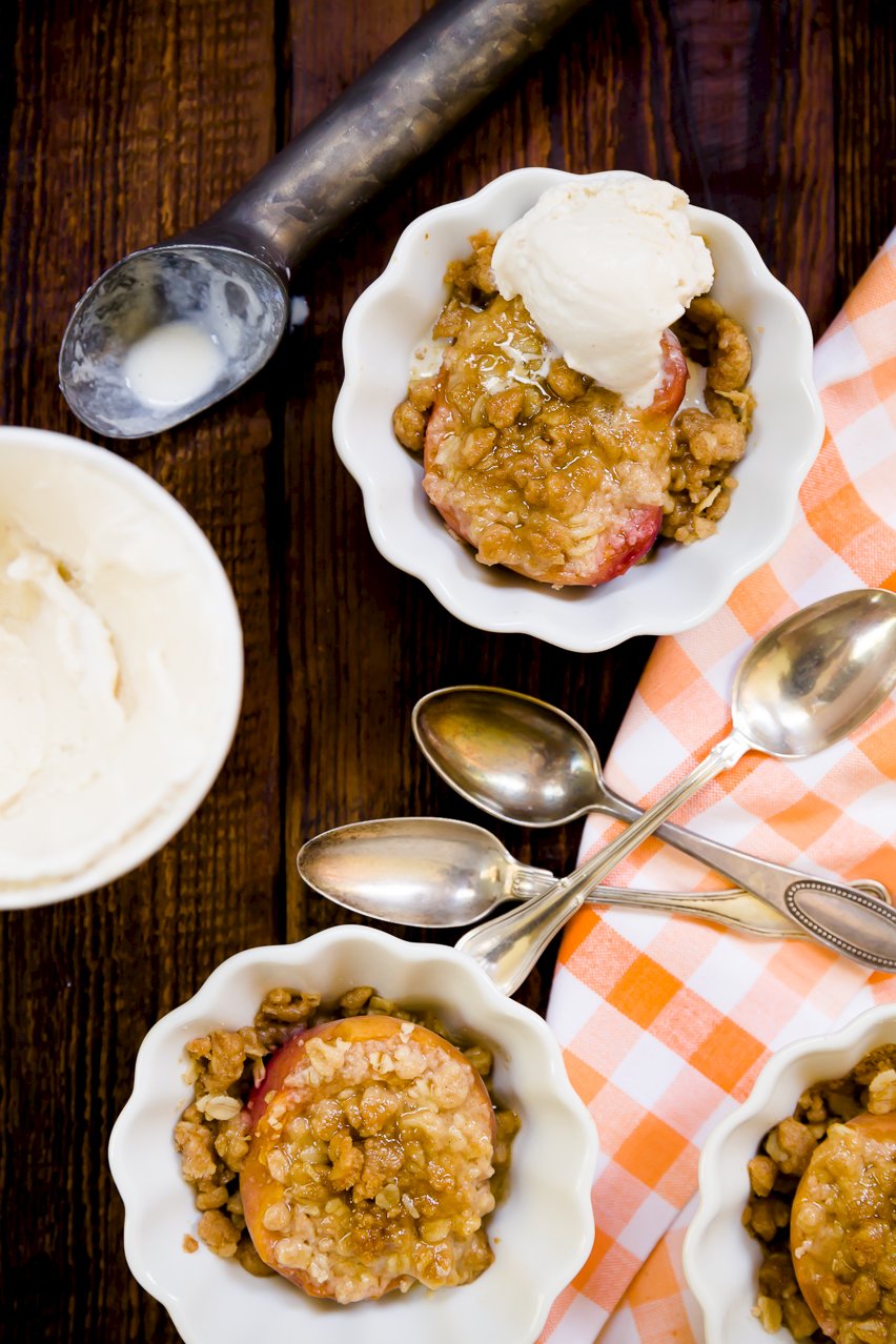 overhead view of baked peaches with crumb topping made in ramekins, topped with ice cream