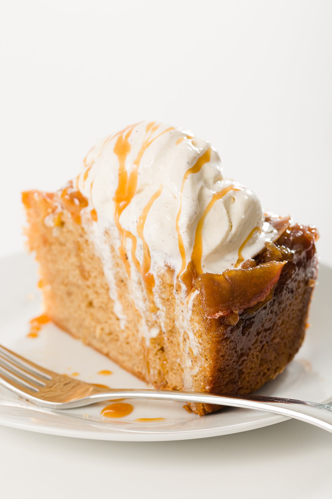 A slice of apple upside-down cake topped with ice cream with caramel drizzled on top