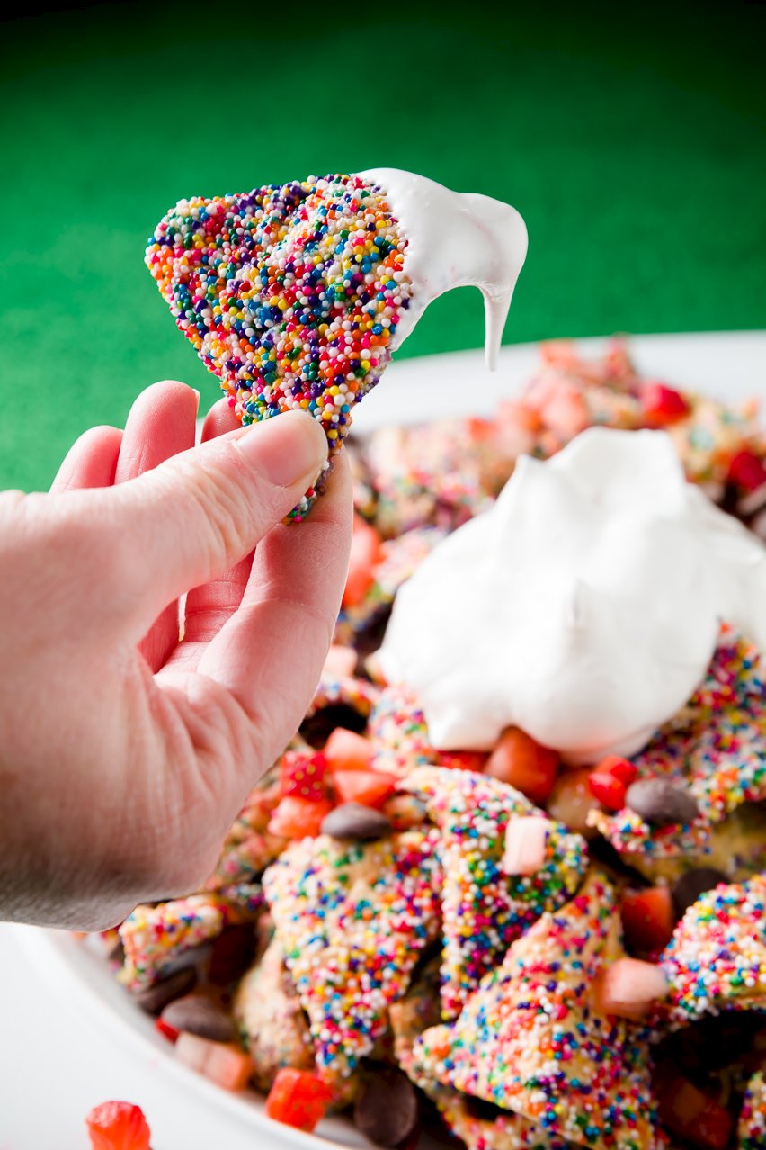 Funfetti Dessert Nachos being held up over a bowl of dessert nachos