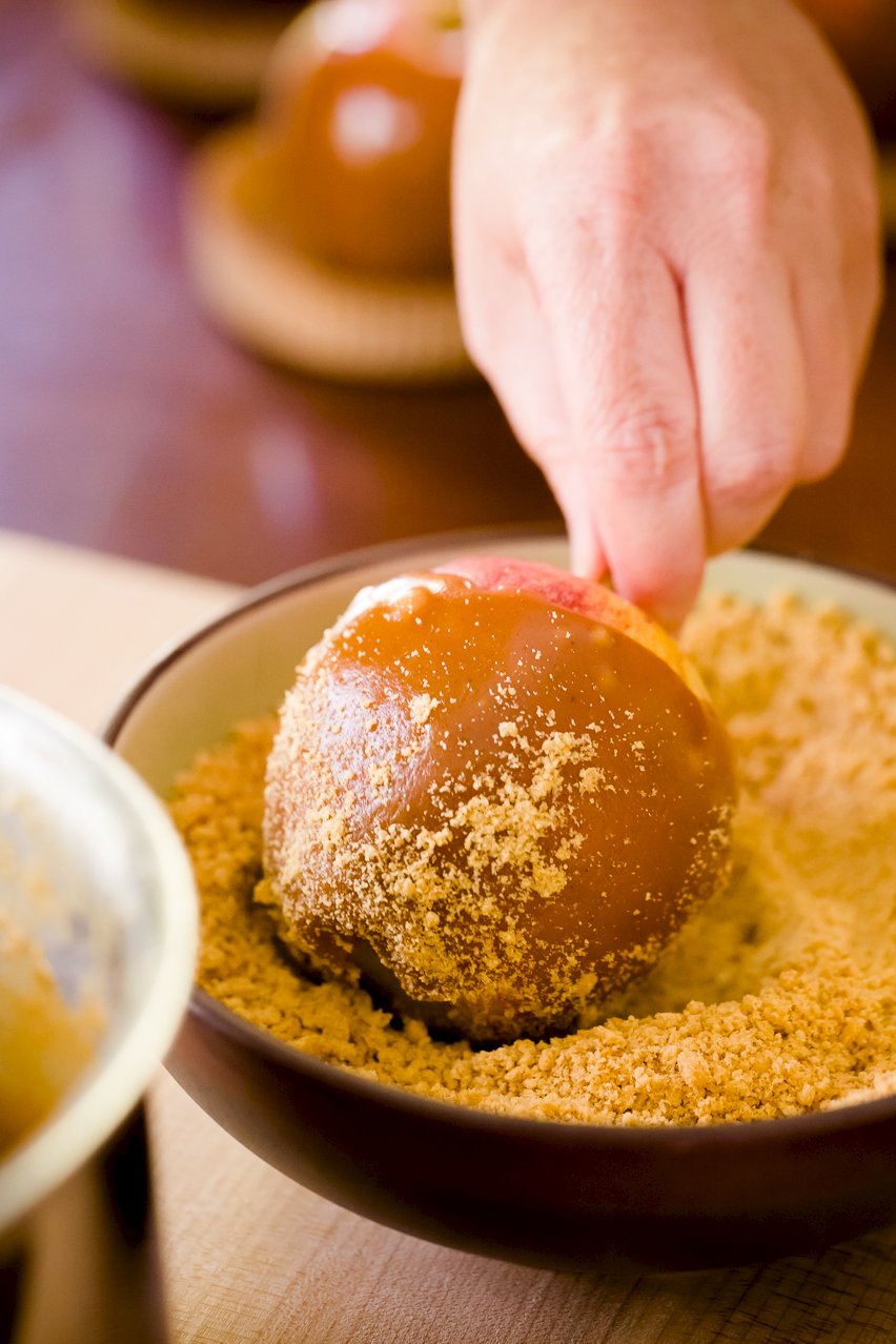 Rolling a caramel apple in graham cracker crumbs