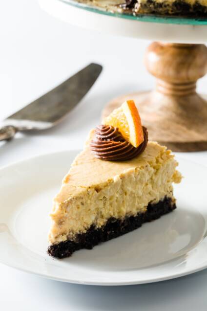 A slice of orange cheesecake with a cake stand in the background