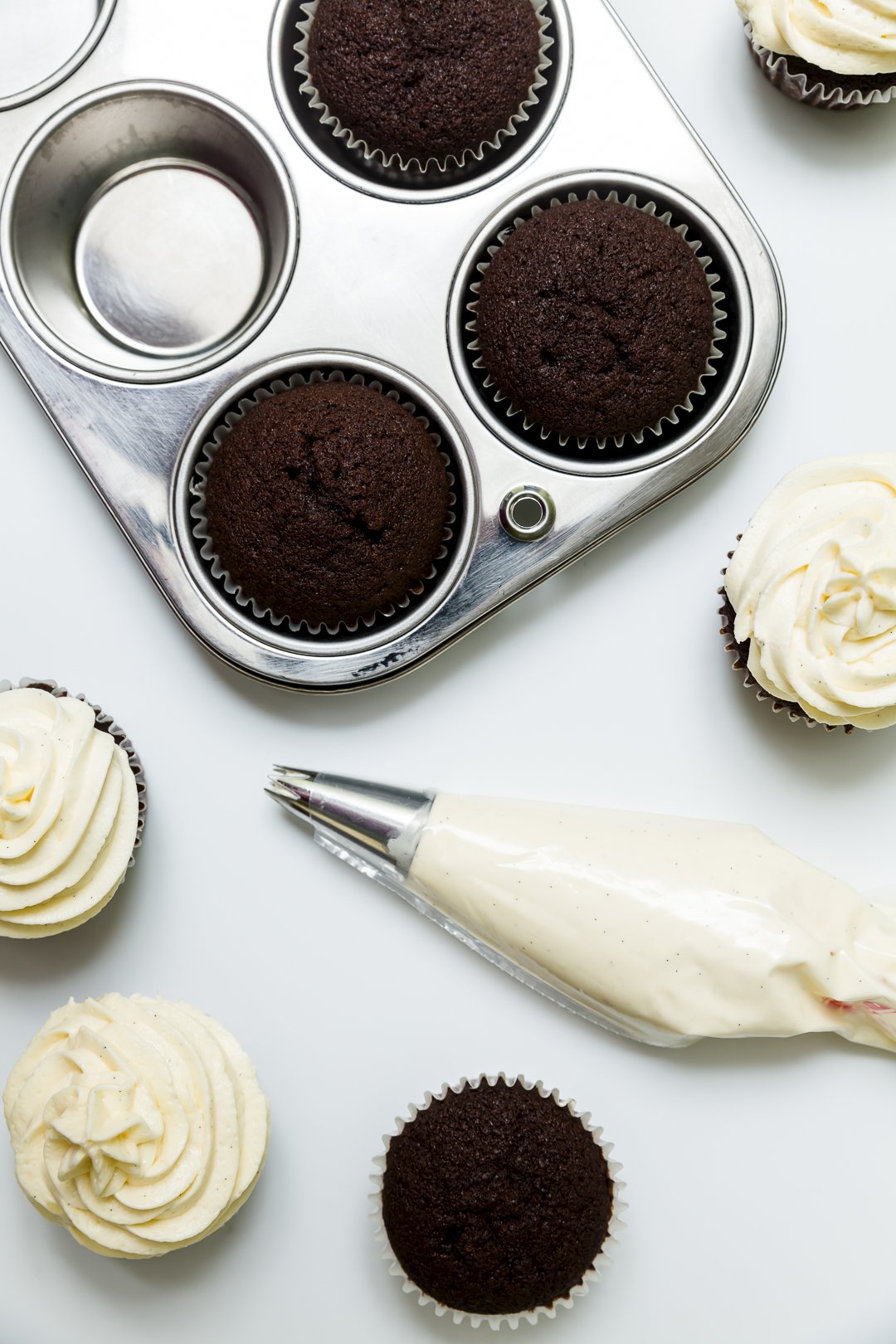 Overhead view of cream cheese frosting in a piping bag sitting near some cupcakes