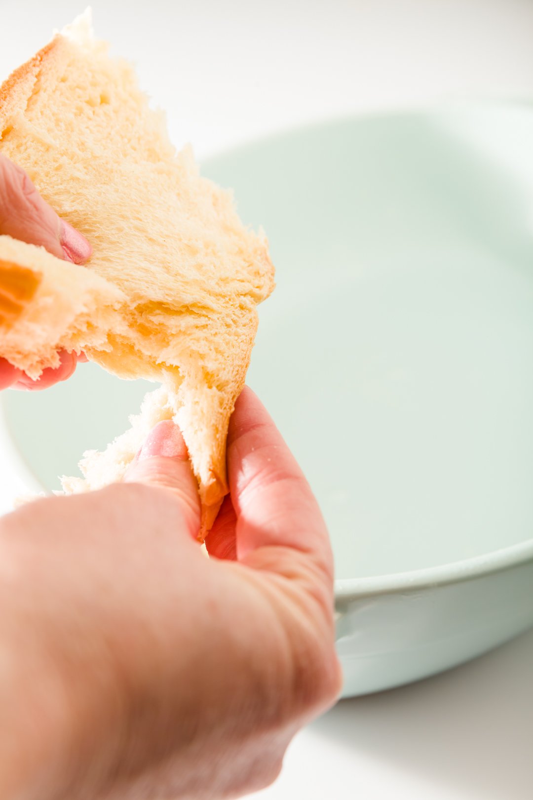 Piece of brioche being ripped over a casserole dish