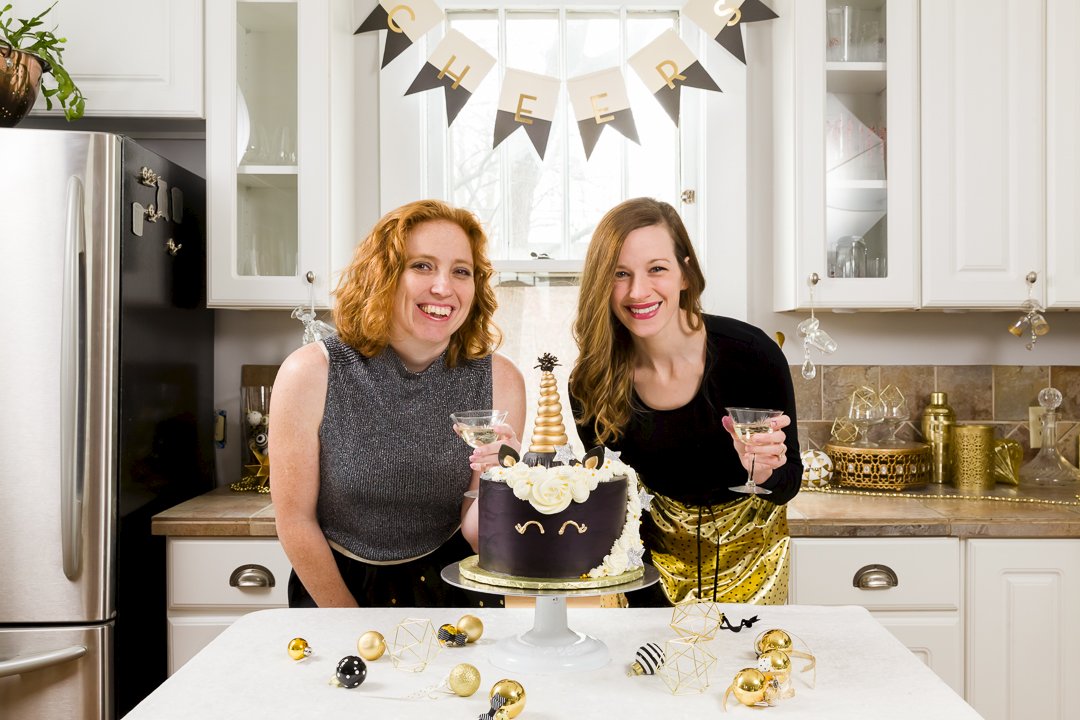 Stef and Lia with champagne glasses behind New Year's Cake