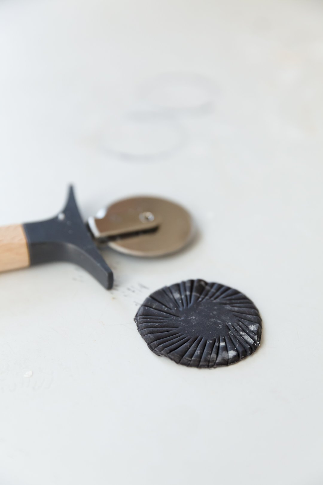 Pastry cutter next a a circle of black fondant with slits in it