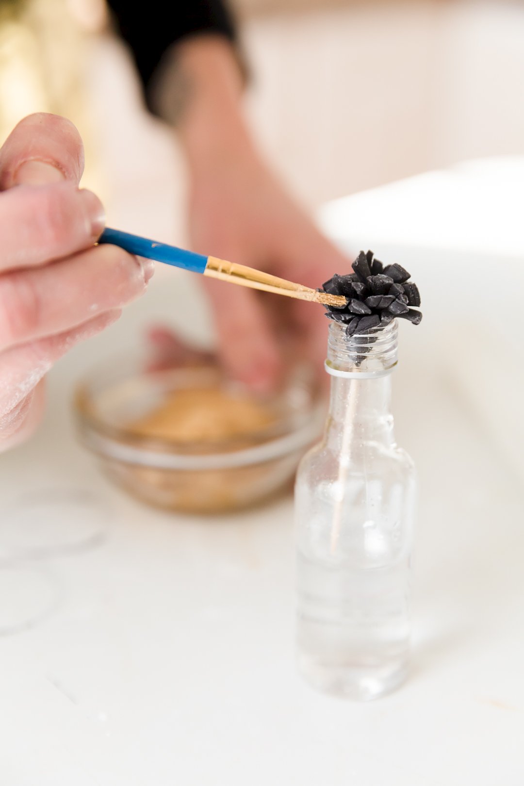 Fondant pom on toothpick in bottle being painted with a brush